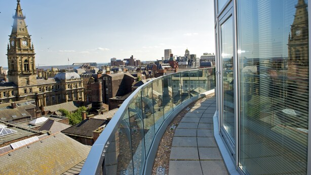 A high-rise building with a curved glass balcony overlooking a cityscape with historic buildings and a clock tower. - PREMIER SUITES Liverpool (Liverpool)