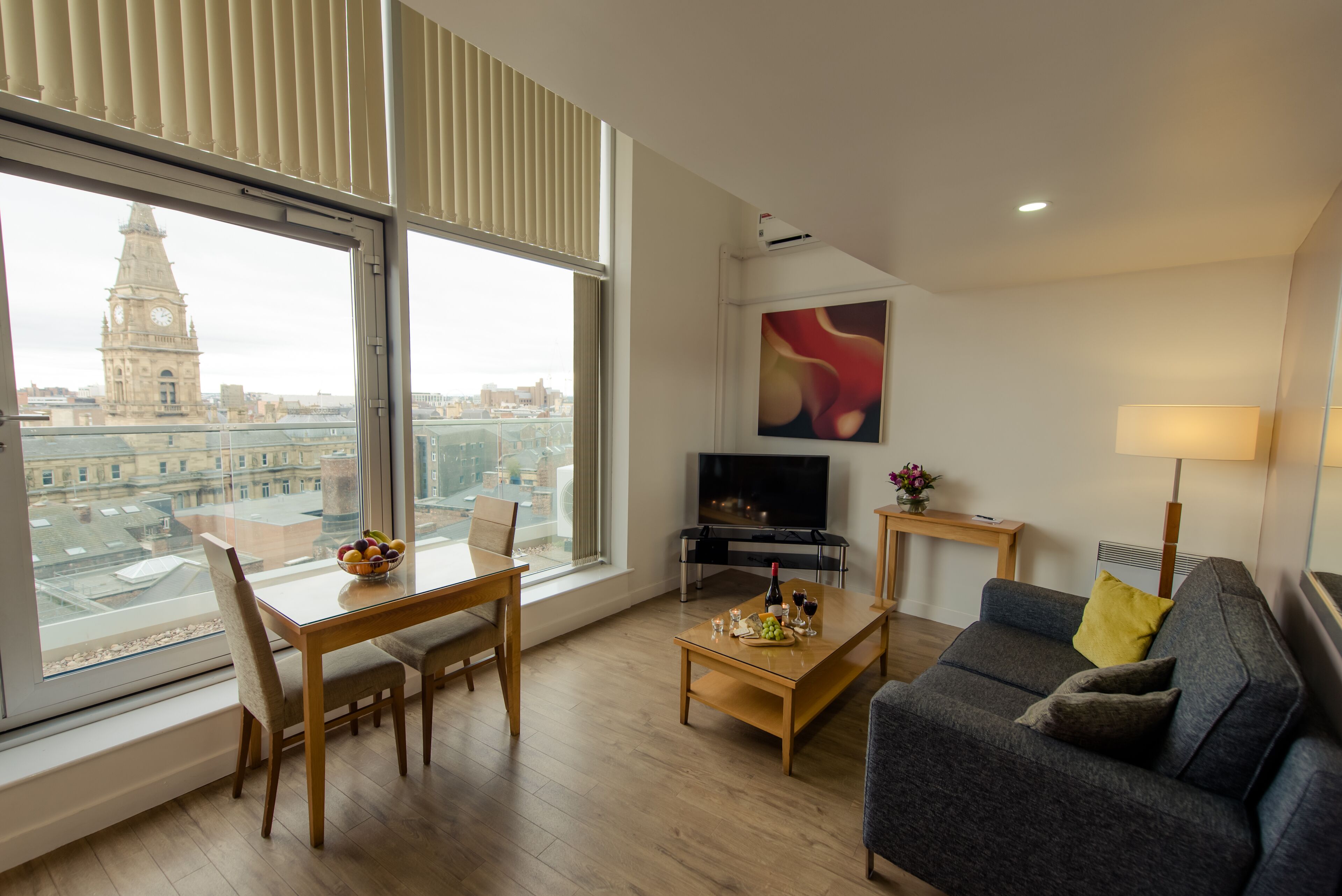 Een moderne woonkamer met een eethoek, grote ramen, een flatscreen televisie en uitzicht op de stad.