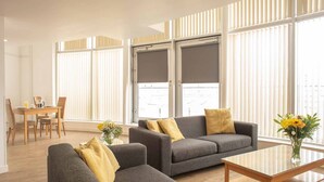 A modern living room with two grey sofas, a wooden coffee table, and a dining area with a table and chairs. - PREMIER SUITES Liverpool (Liverpool)