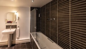 A modern bathroom with a white sink, a mirror, and a bathtub. - PREMIER SUITES Liverpool (Liverpool)