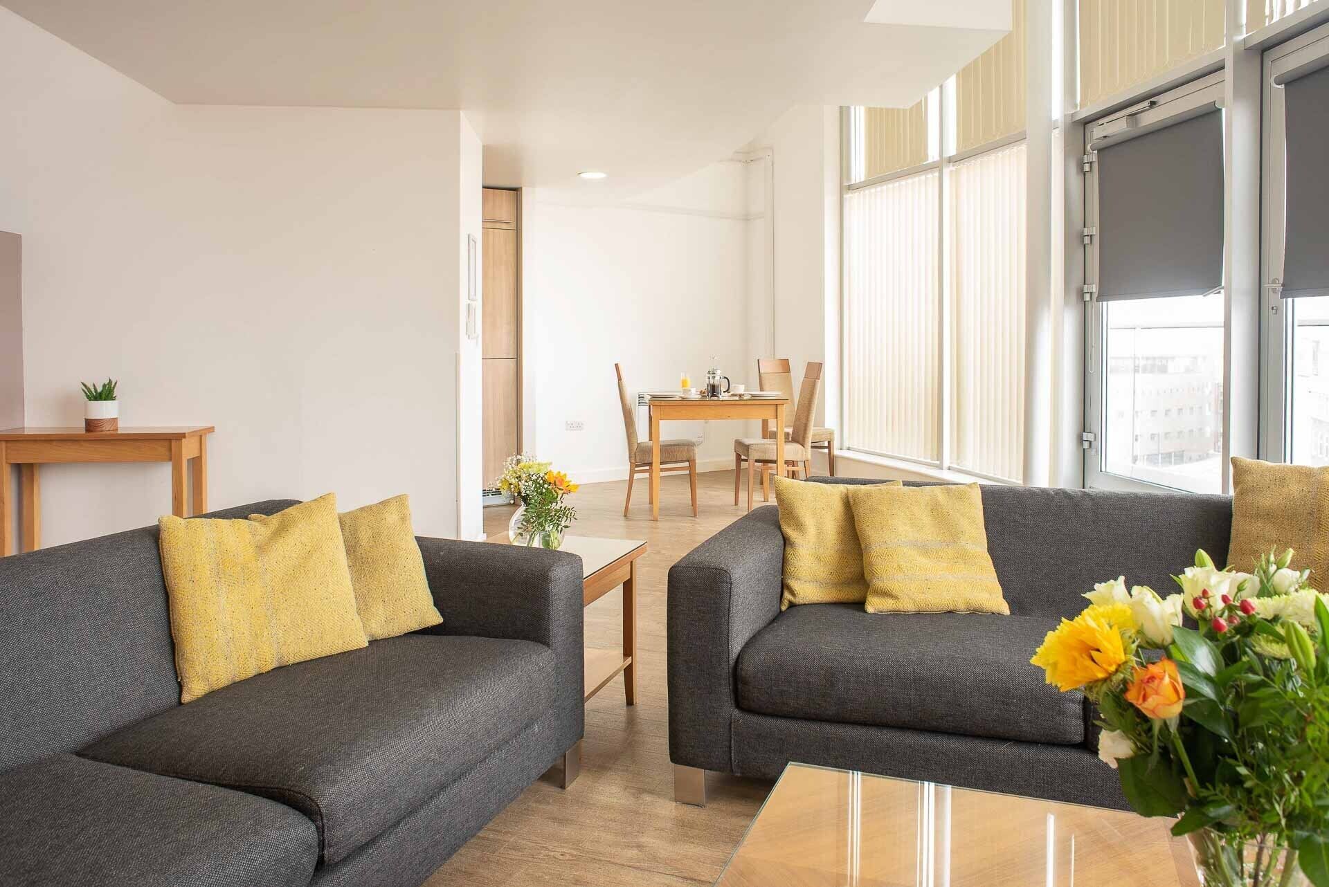 Una sala de estar moderna con dos sofás grises, una mesa de centro de madera y un comedor con una mesa y sillas de madera.