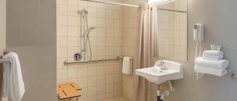 A small, single-room bathroom with a shower, a sink, a mirror, and a telephone.