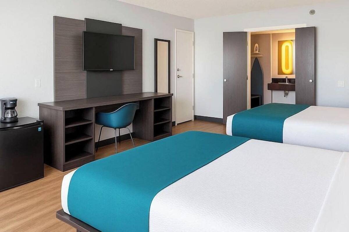A hotel room with two beds, a desk, a chair, a TV, and a coffee maker.