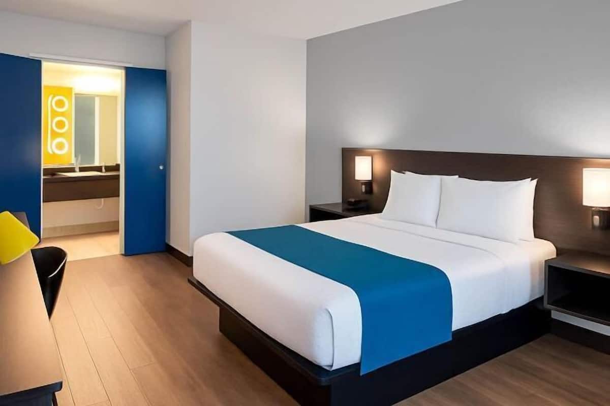 A modern hotel room with a large bed, bedside lamps, and a bathroom with a mirror and sink.