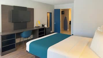 Una habitación de hotel con cama, escritorio, silla, televisor y armario.