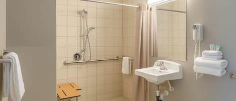 Un baño con ducha, lavamanos, espejo y toallero.