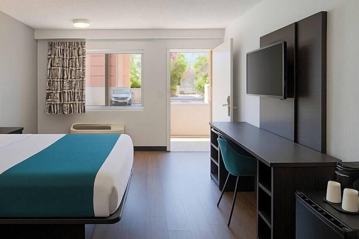 A hotel room with a bed, a desk, a TV, and a window with a view of the outside.