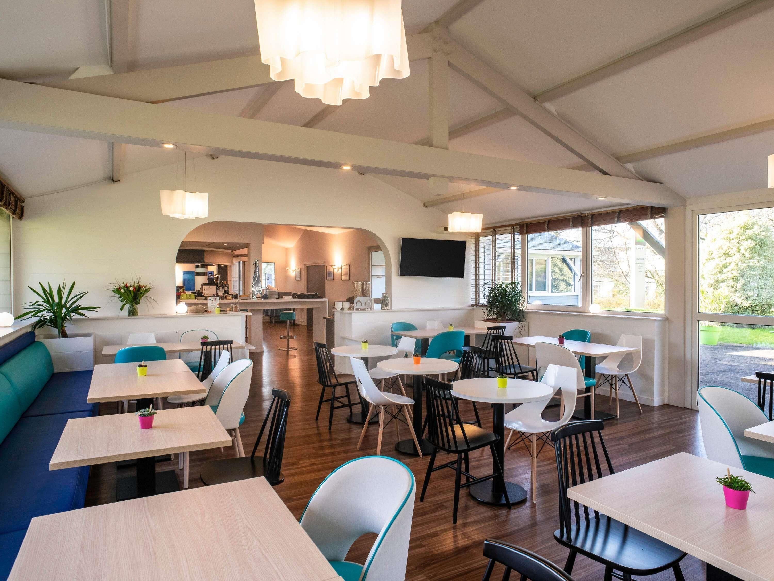 A modern restaurant with high ceilings, natural light, and a mix of seating options including tables and booths.