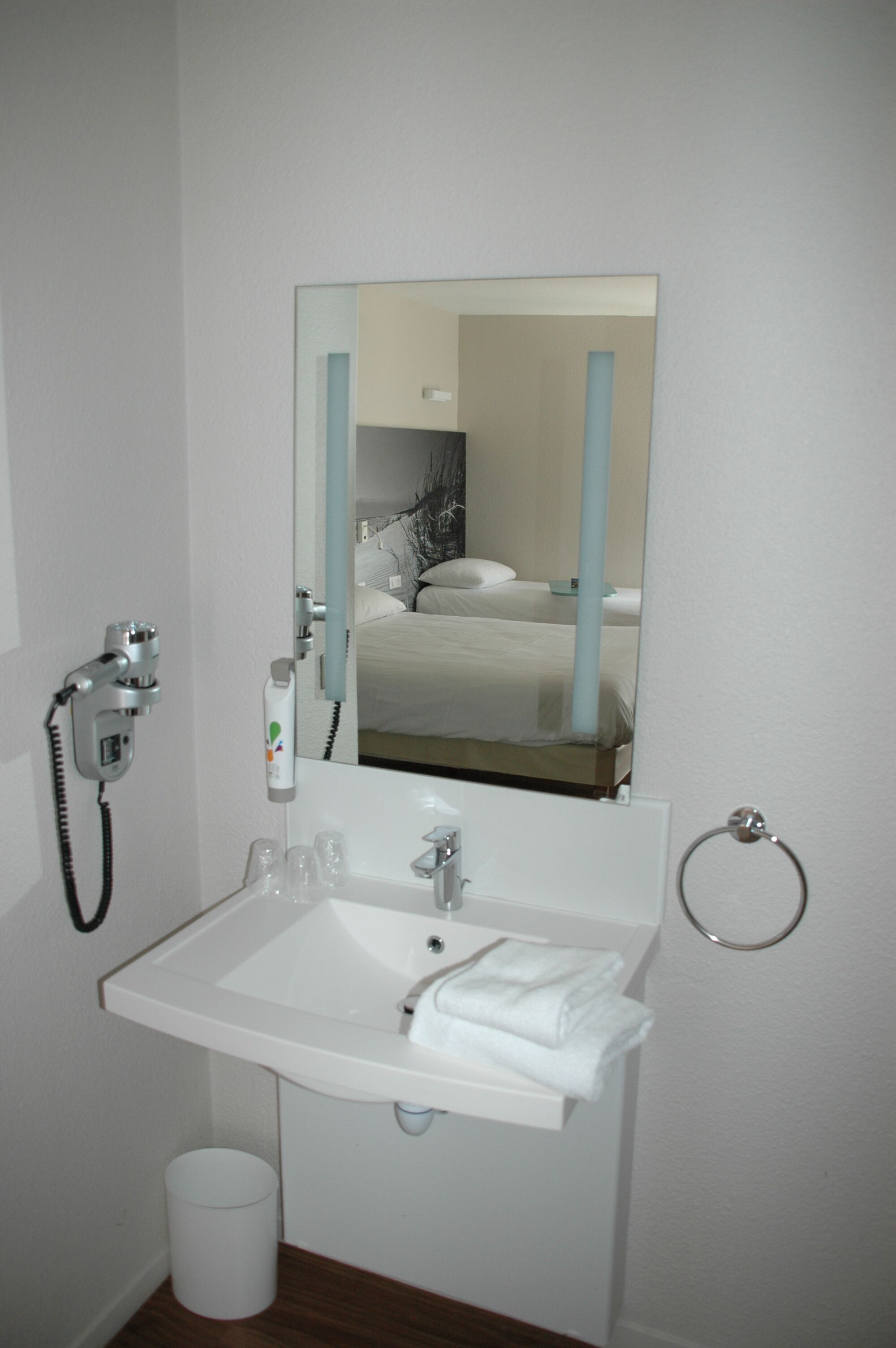 A hotel bathroom with a sink, mirror, and a towel rack.