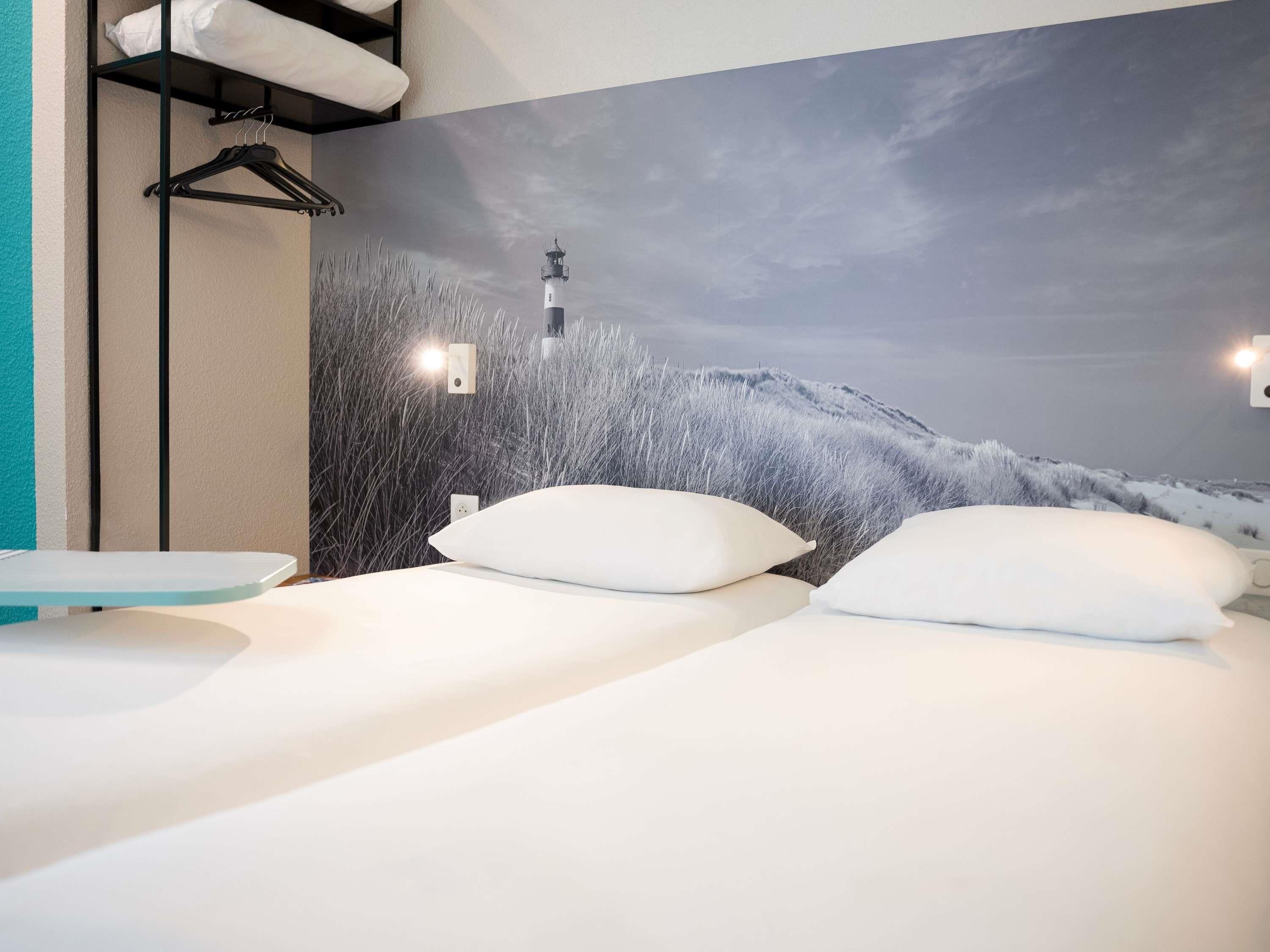 Une chambre avec deux lits, une étagère fixée au mur et une fresque représentant un phare.