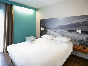 A hotel room with a bed, a nightstand, a wall-mounted lamp, and a beach-themed mural. - ibis Styles Quimper (Quimper)