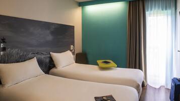 A hotel room with two beds, a nightstand, a lamp, and a window with curtains.
