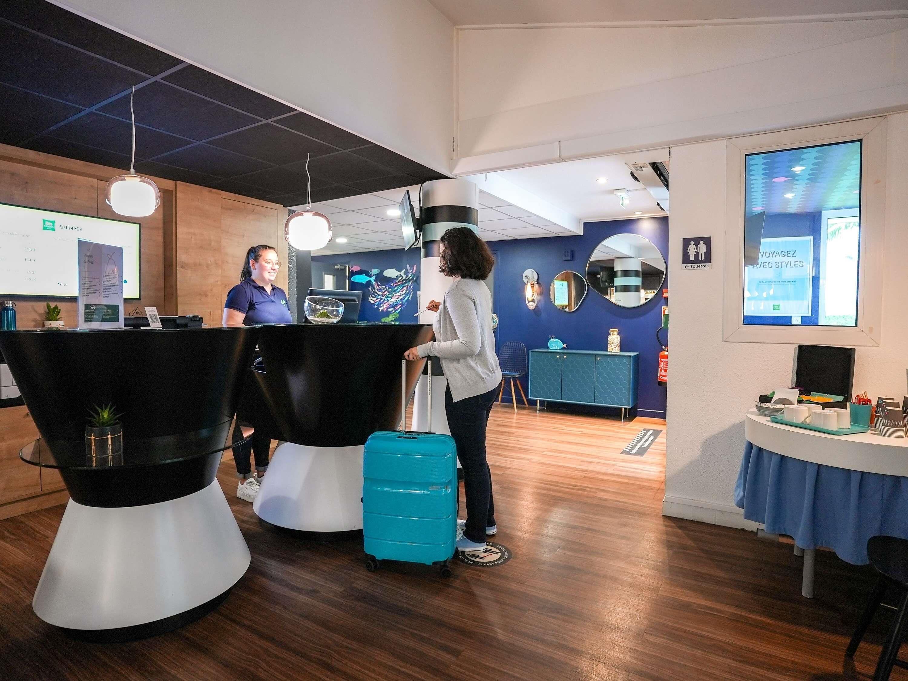 A hotel lobby with a reception desk, a large aquarium, and a blue wall with a mirror and a digital screen.