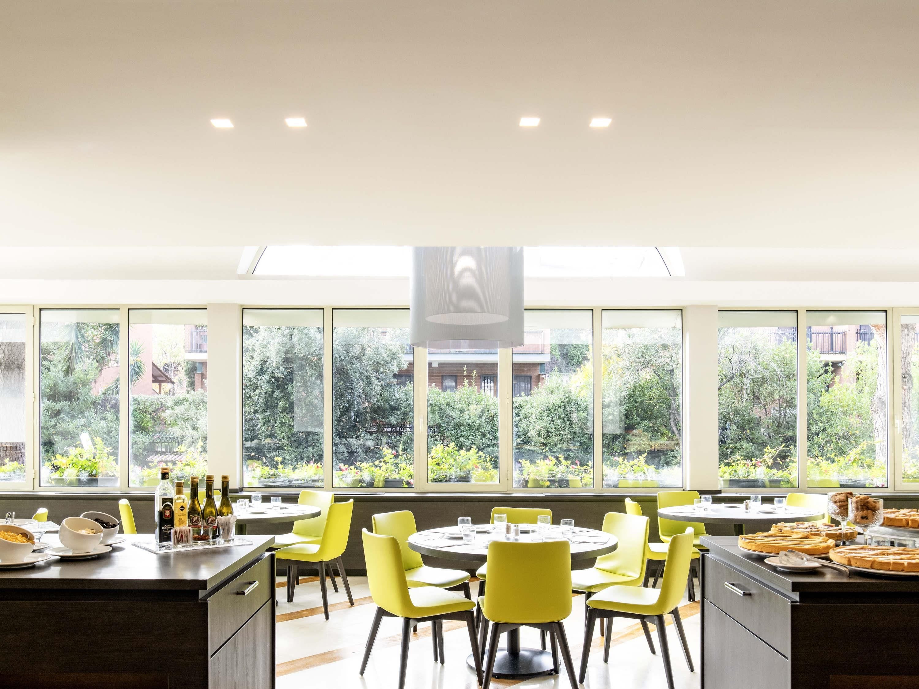 A modern dining area with yellow chairs, round tables, and a view of greenery outside.