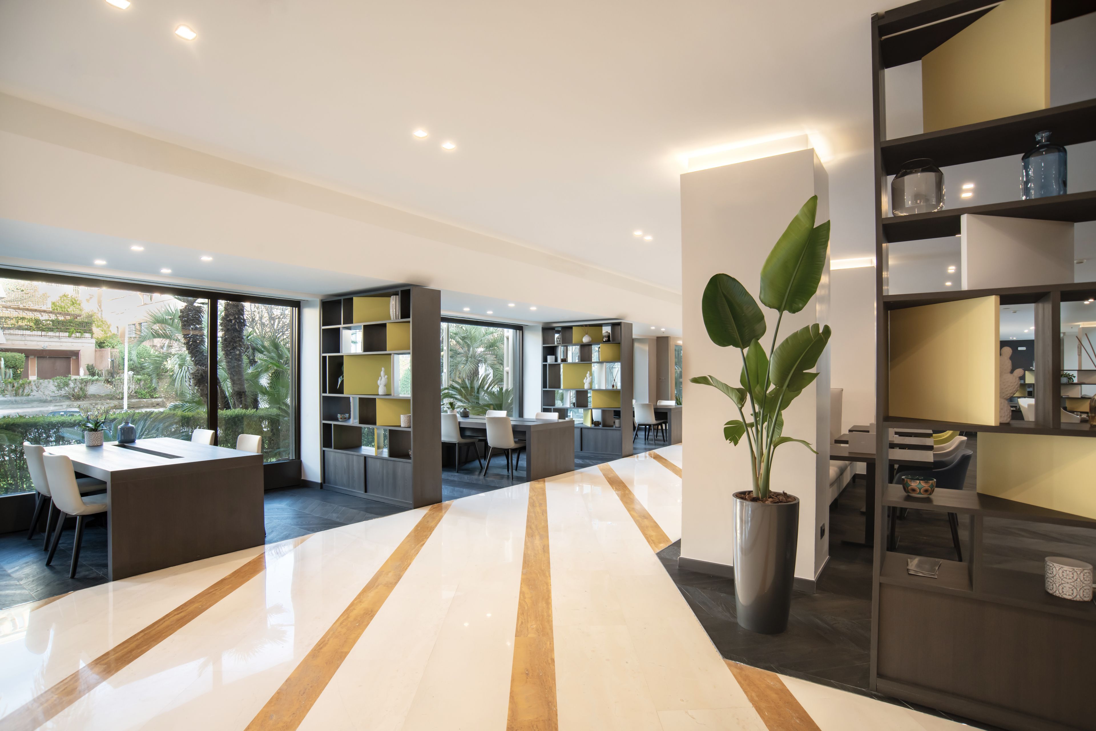 Un interior moderno con piso pulido y brillante, un área de estar central con mesas y sillas, y una gran planta en maceta.