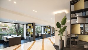 A modern interior with a long, polished floor, a central seating area with tables and chairs, and a large potted plant. - Mercure Eur Roma West (Rome)