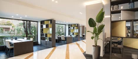 Un interior moderno con piso pulido y brillante, un área de estar central con mesas y sillas, y una gran planta en maceta.