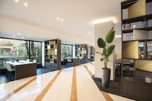 A modern interior with a long, polished floor, a central seating area with tables and chairs, and a large potted plant. - Mercure Eur Roma West (Rome)
