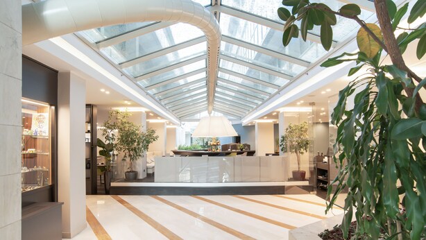 A spacious indoor area with a high ceiling and a glass roof, featuring a central island with seating and a large lamp. - Mercure Eur Roma West (Rome)