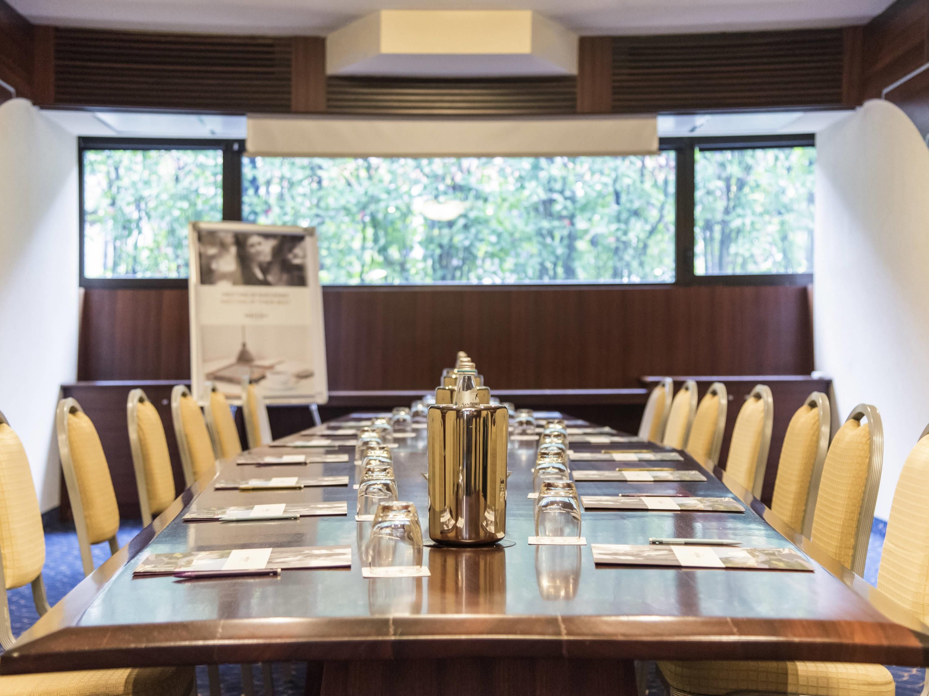 A conference room with a long table, chairs, a projector screen, and a poster.