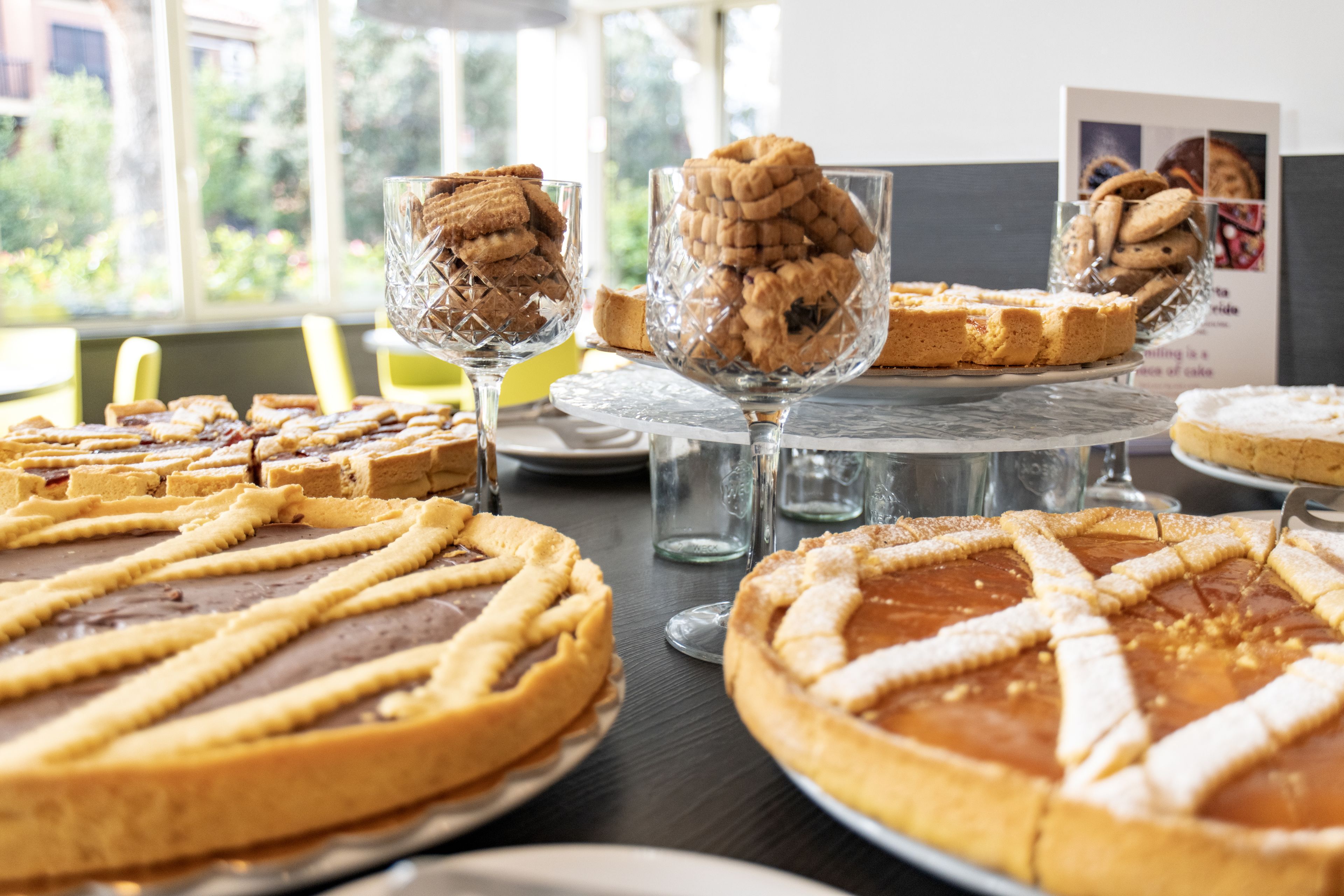 Verschiedene Desserts auf einem Tisch, darunter Kuchen und Kekse, mit Blick aus dem Fenster im Hintergrund.