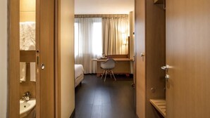 A hotel room with a bed, desk, chair, and a bathroom with a sink and toilet. - Mercure Eur Roma West (Rome)