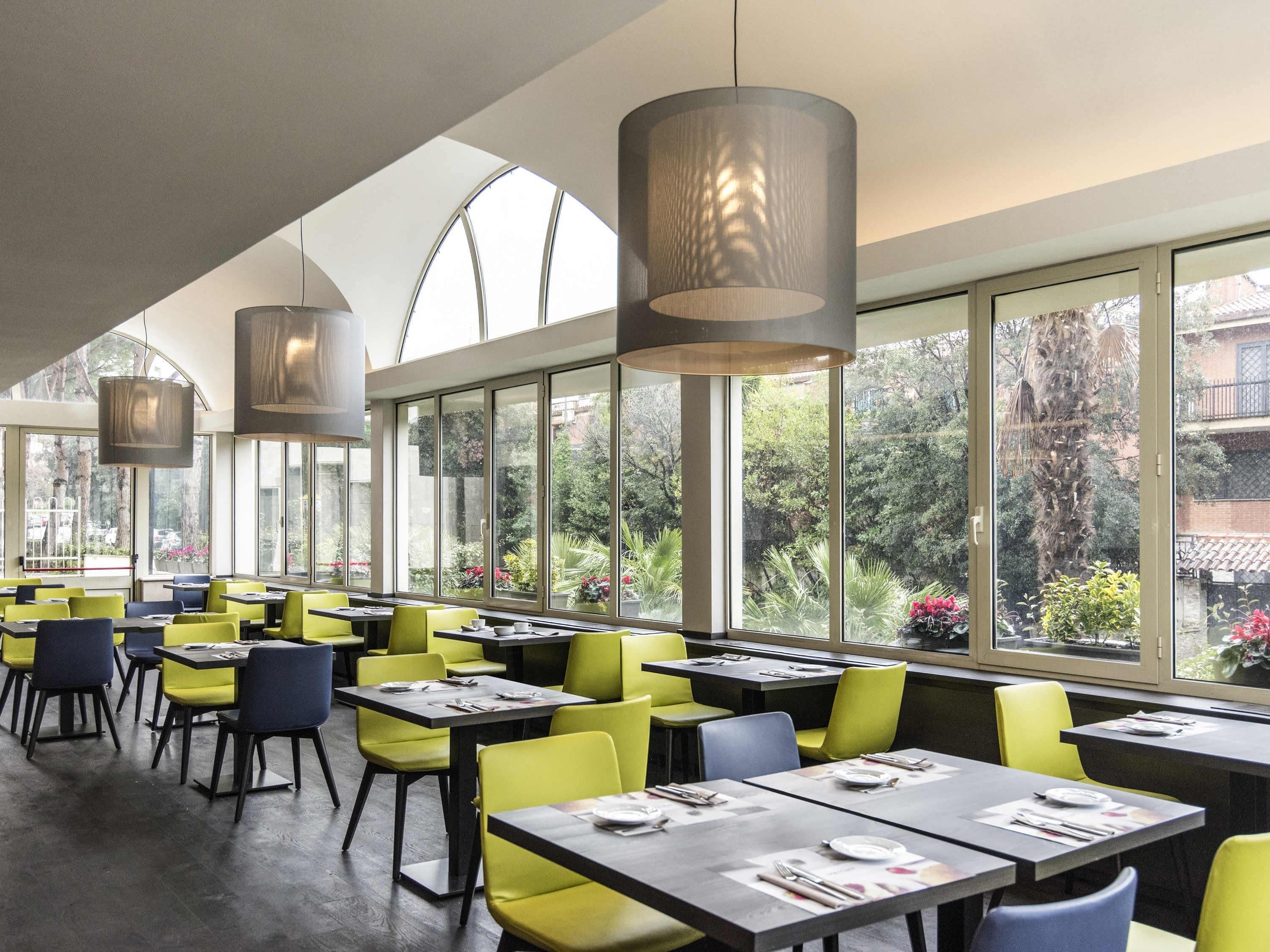 Een restaurant met tafels, stoelen, grote ramen en hangende lampen.