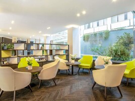 A modern indoor space with a wooden herringbone floor, a central seating area with yellow and white chairs, and a bookshelf with various decorative items.