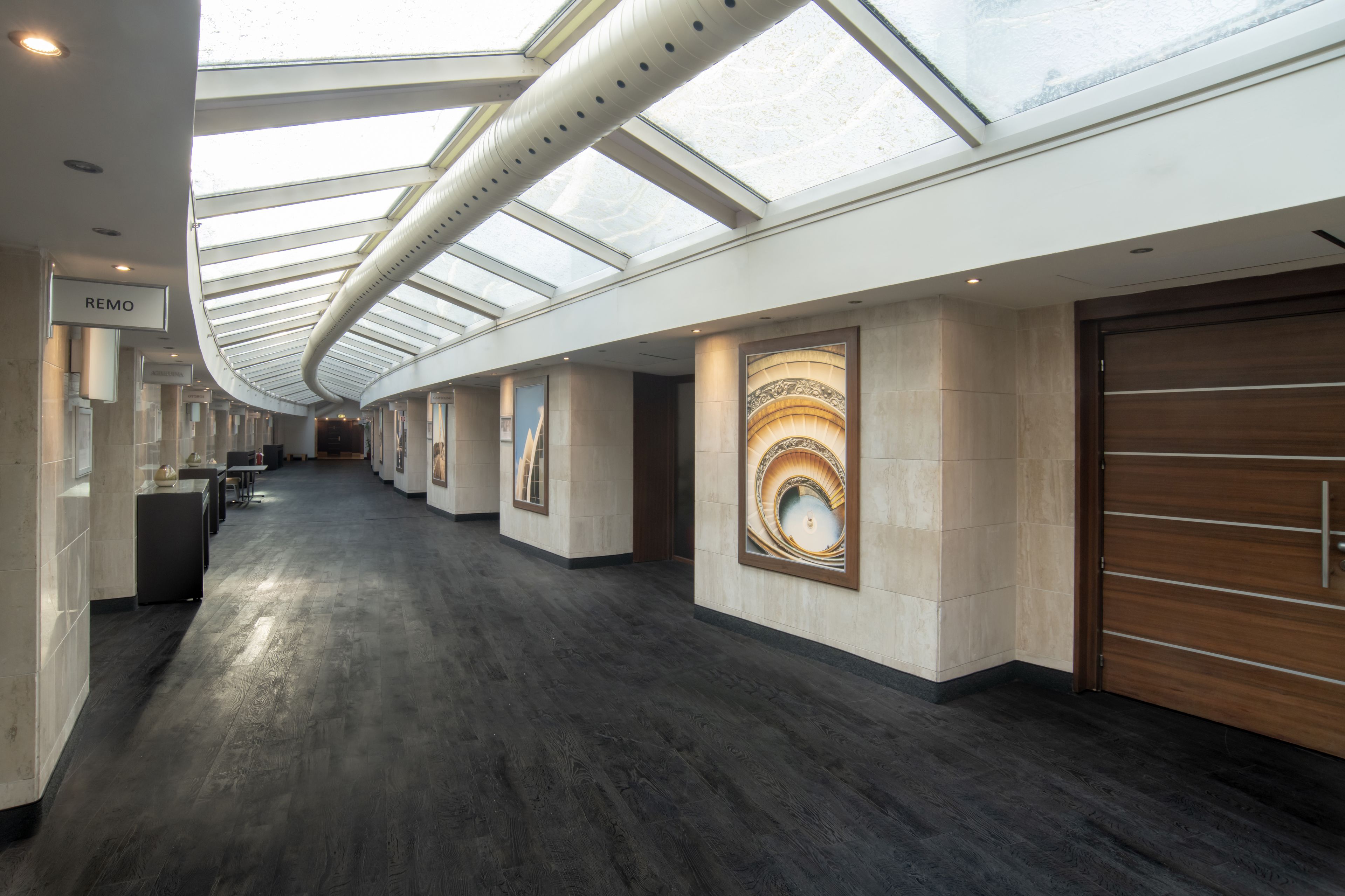 A modern hotel corridor with a skylight, artwork on the walls, and a sign reading "REMO".