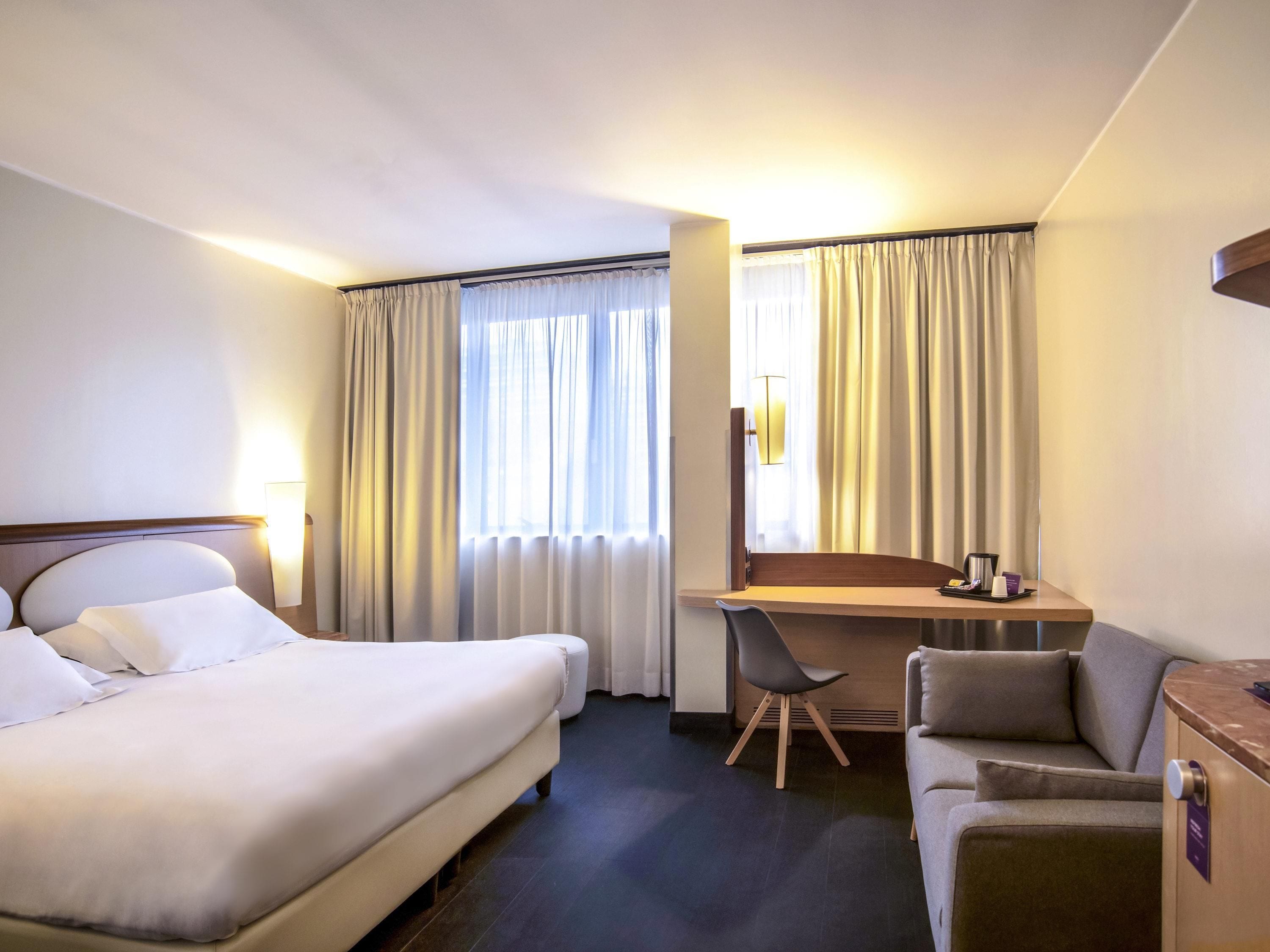A hotel room with a bed, a desk, a chair, and a sofa.