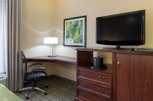 A hotel room with a desk, chair, television, and a cabinet.