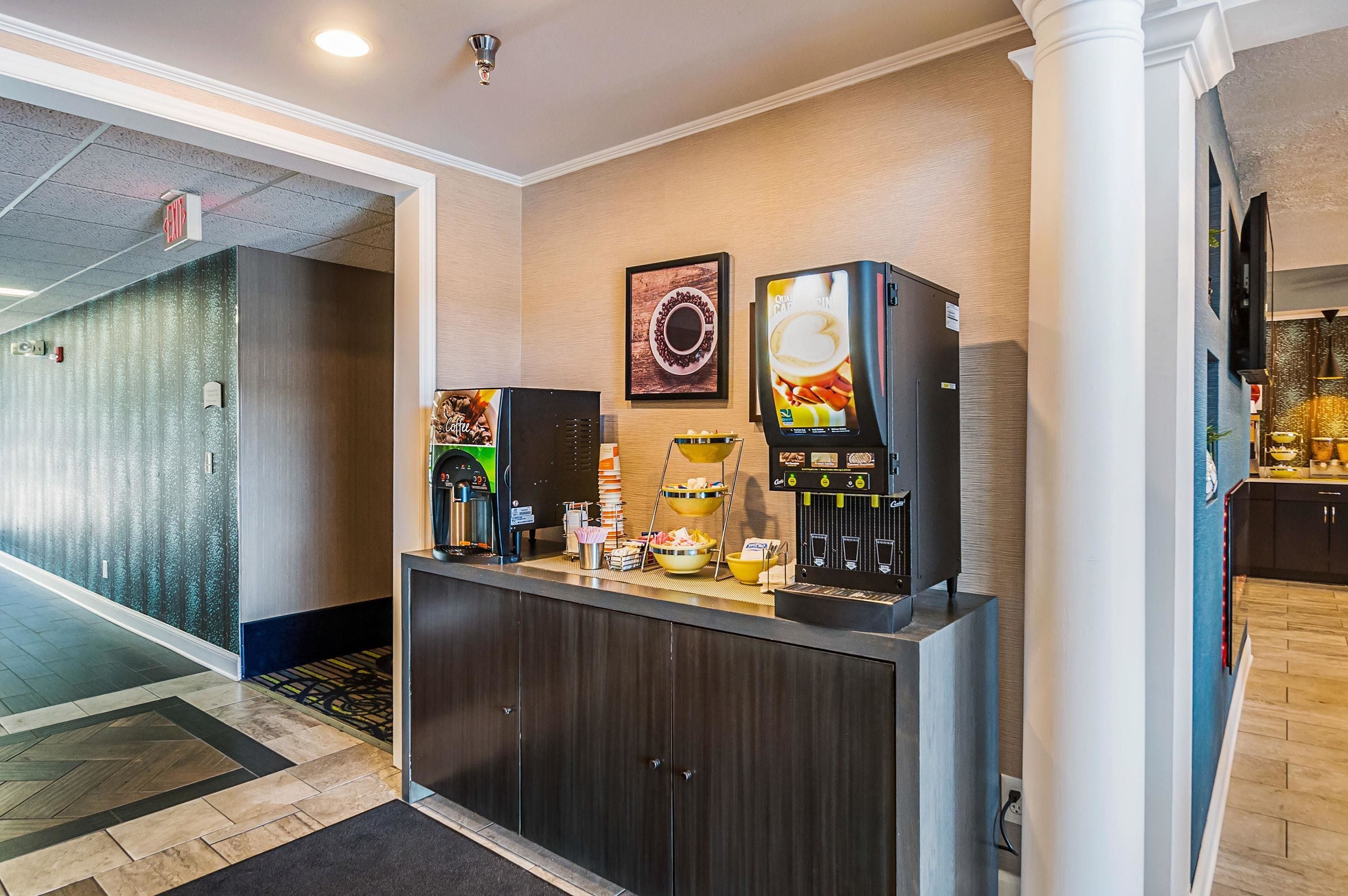 A hotel reception area with a coffee machine, a beverage dispenser, and a framed picture on the wall.