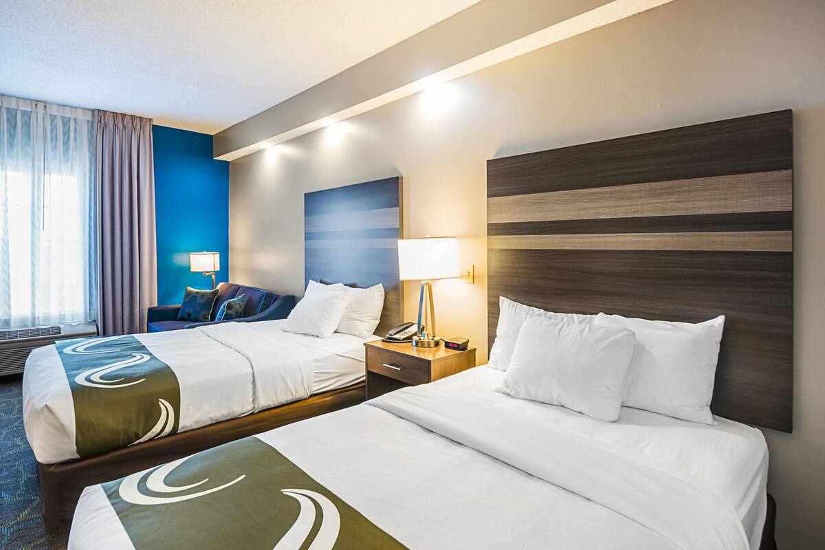A hotel room with two beds, a nightstand with a lamp, a telephone, and a wall-mounted artwork.