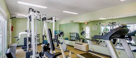 A gym with various exercise machines, a treadmill, and a mirrored wall.