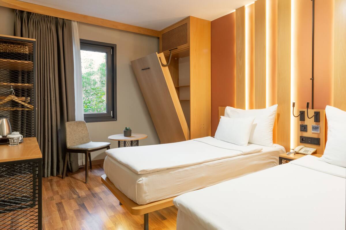 A hotel room with two beds, a desk, a chair, a small table, and a window with curtains.