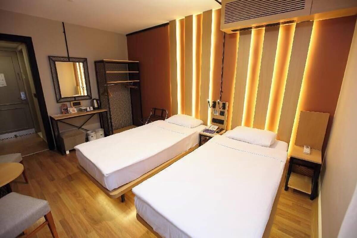 A hotel room with two single beds, a desk, a chair, a mirror, a wardrobe, and a bedside table.