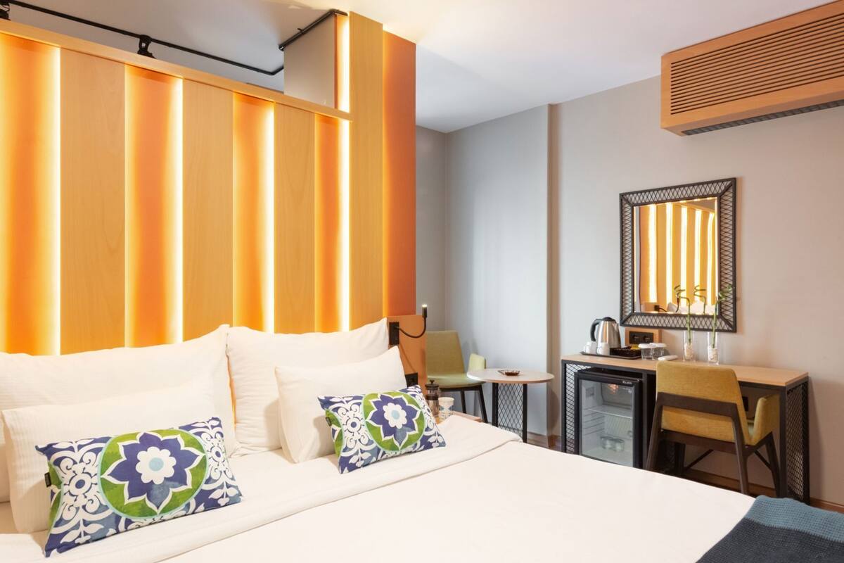 A hotel room with a bed, a desk, a chair, a mirror, and a radiator.