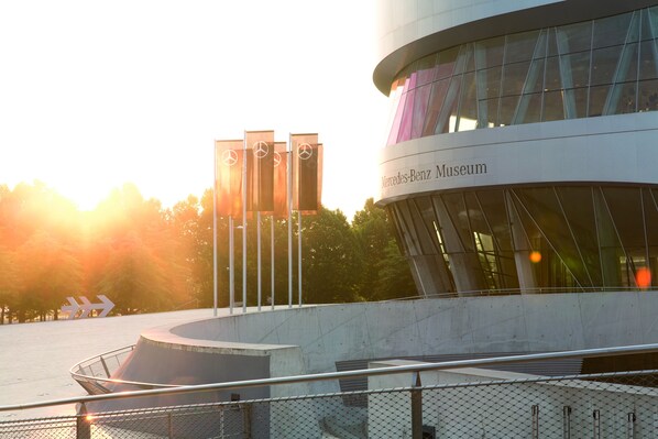 El exterior del Museo Mercedes-Benz, con un diseño arquitectónico moderno, que presenta grandes ventanales de vidrio y una estructura curva destacada.
