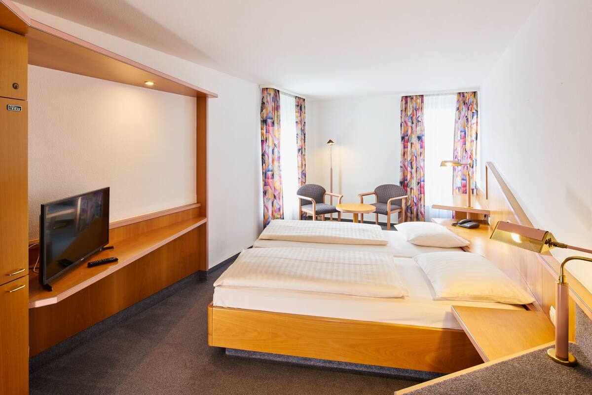 A hotel room with a bed, a desk with a chair, a television, and a lamp.