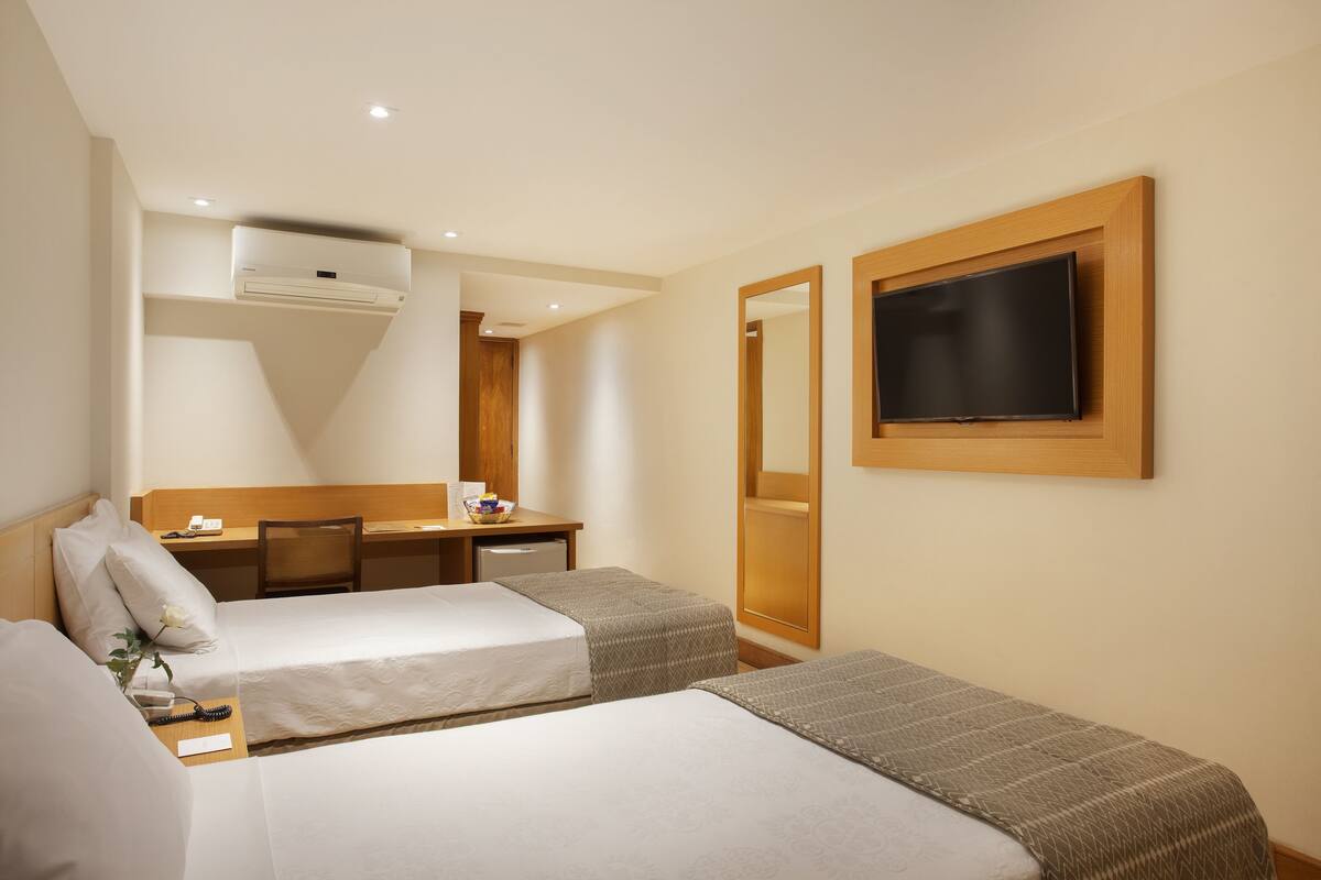 Ein Hotelzimmer mit zwei Betten, einem Schreibtisch, einem Stuhl, einem Fernseher und einer Klimaanlage.
