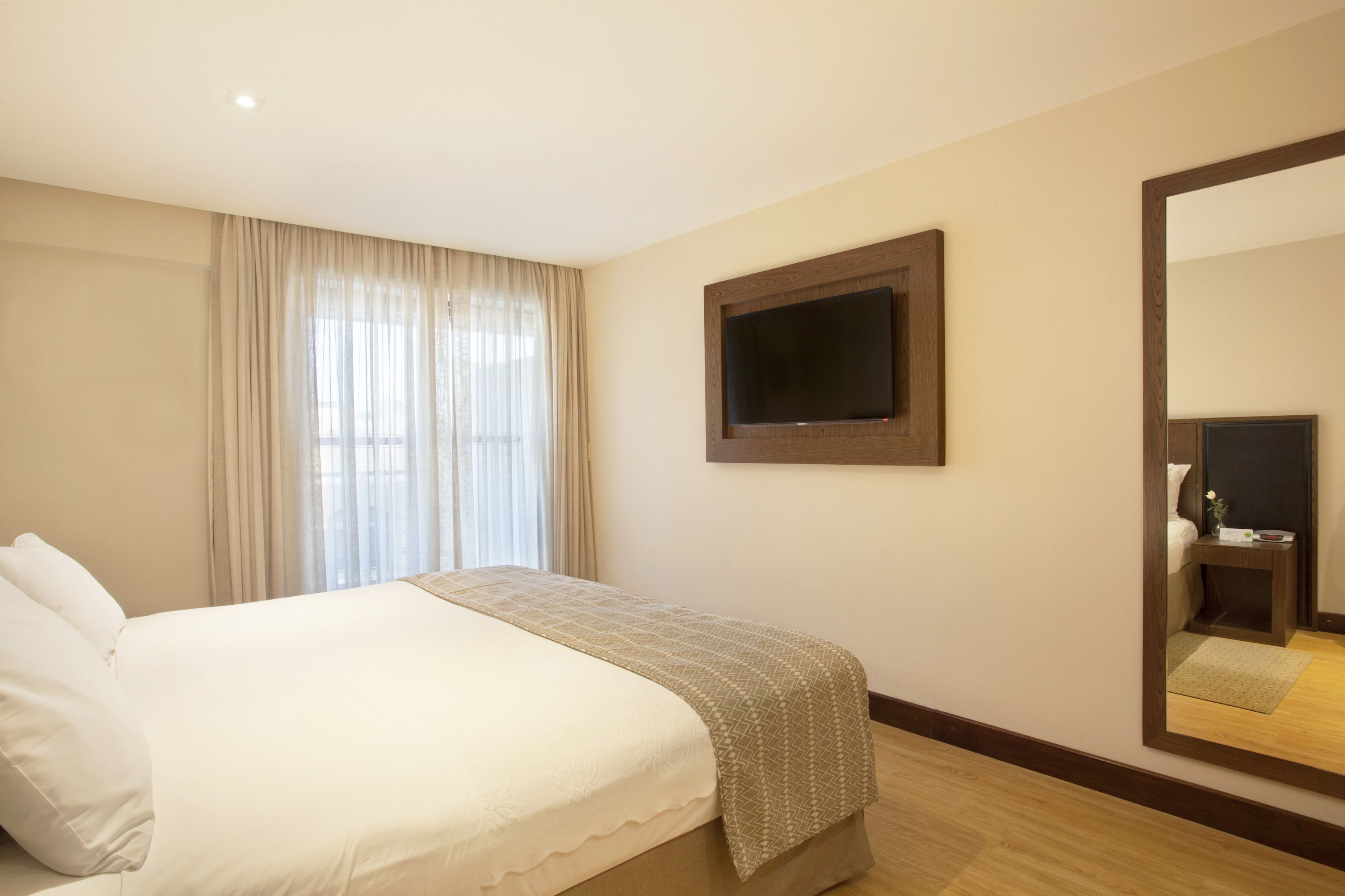 A hotel room with a bed, a television mounted on the wall, and a large mirror.