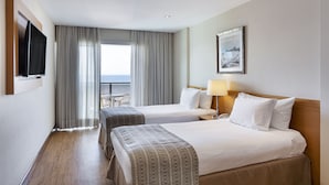 Habitación de hotel con dos camas, televisor, un cuadro y vista al mar.