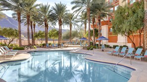 A pool area with lounge chairs and umbrellas, surrounded by palm trees and a building with balconies. - Fiesta Henderson Hotel and Casino (Henderson)