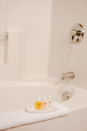 A bathroom with a white bathtub, a white towel, and three bottles of toiletries on the edge. - Fiesta Henderson Hotel and Casino (Henderson)