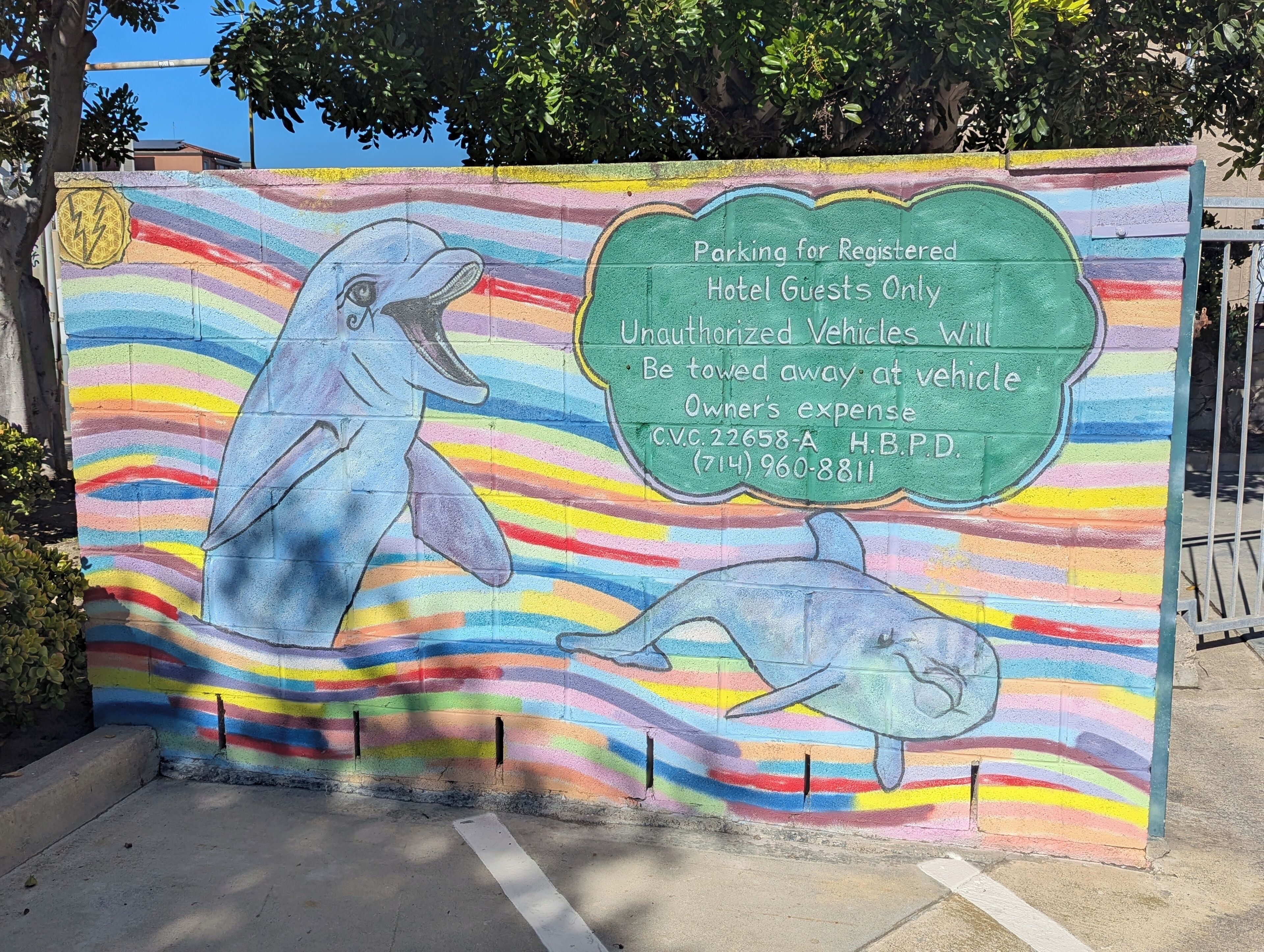 A colorful mural with dolphins and a parking sign for registered hotel guests, warning unauthorized vehicles will be towed.