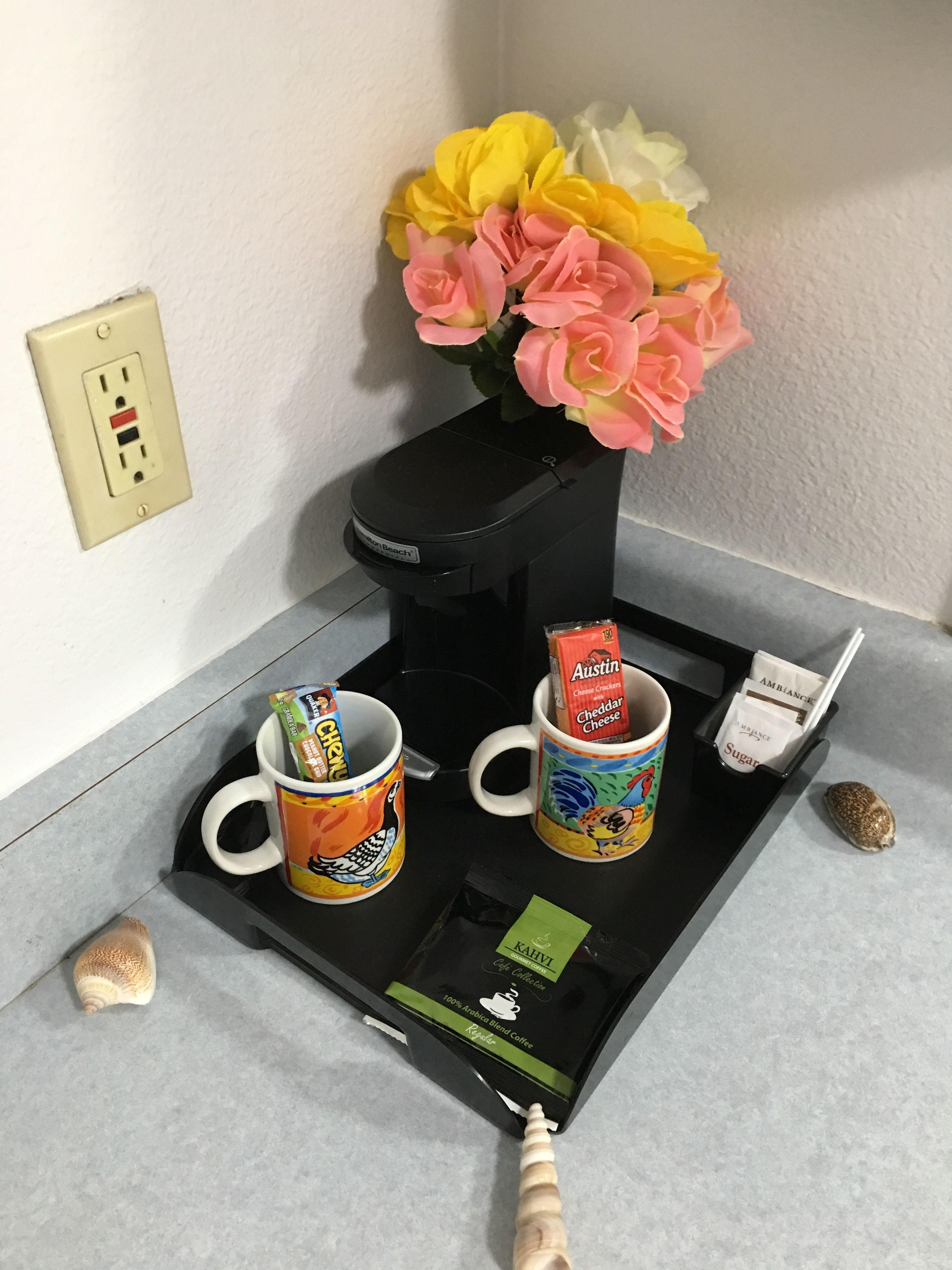 A coffee station with two mugs, a coffee maker, and a flower arrangement.