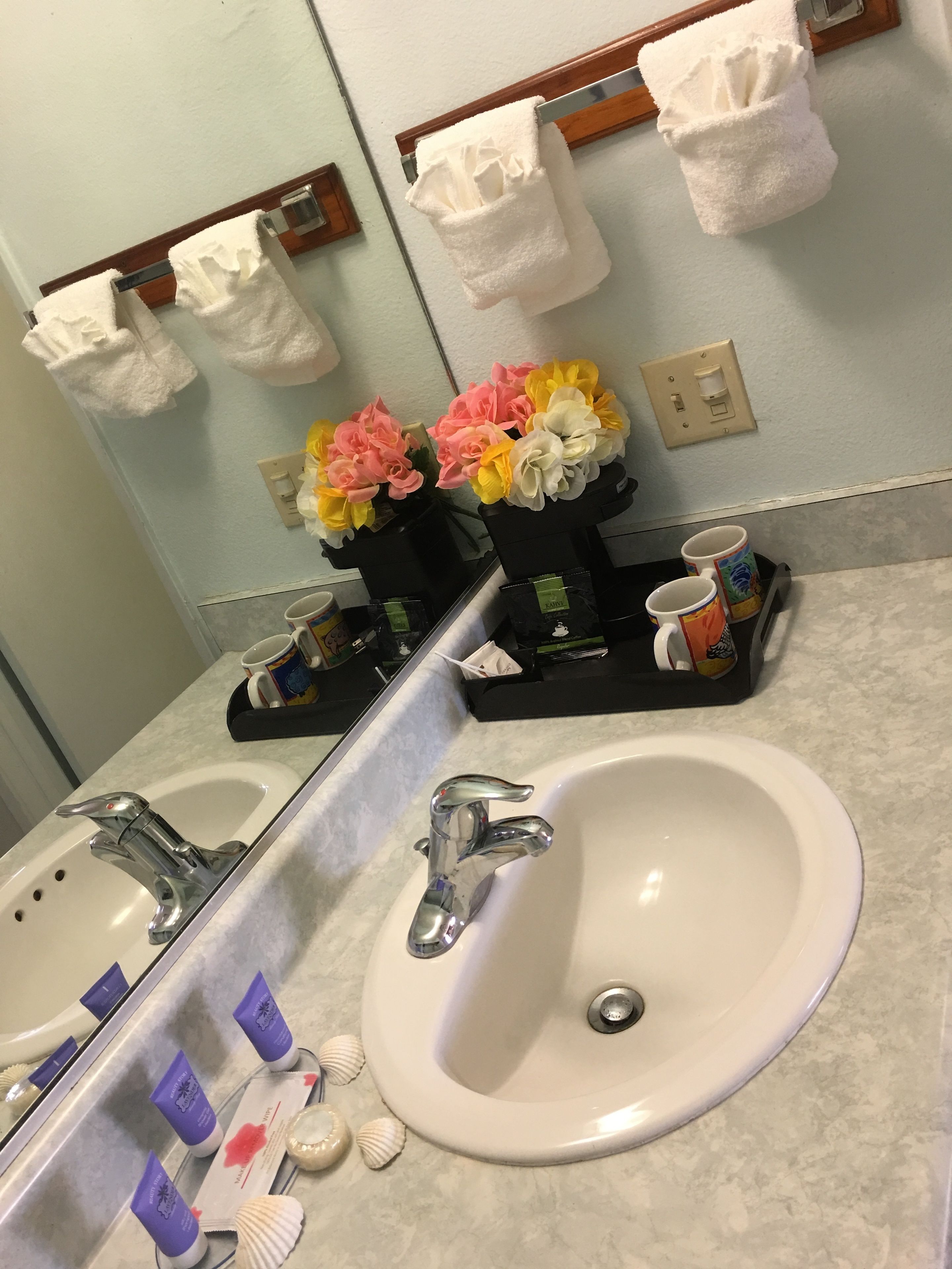 A bathroom with a sink, two towel racks, a mirror, and a shelf with toiletries and decorative flowers.