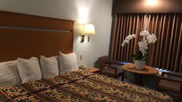 A hotel room with a large bed, a desk with a lamp, a chair, and a potted orchid plant.
