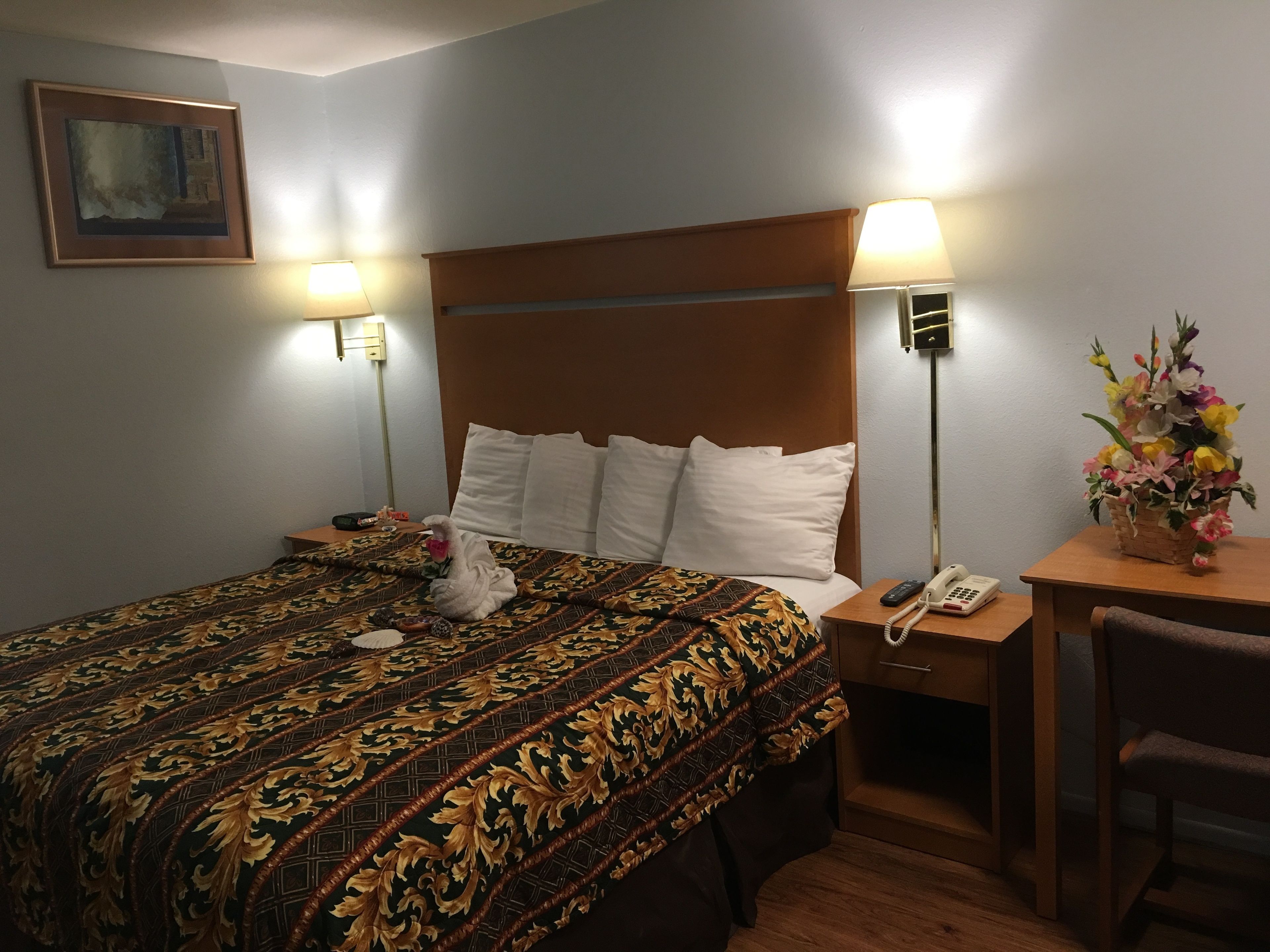 A hotel room with a large bed, two bedside lamps, a bedside phone, a small table with a vase of flowers, and a chair.