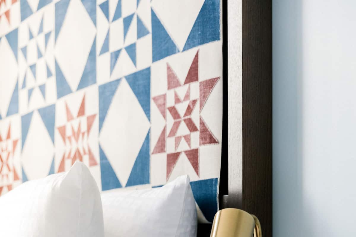 A neatly made bed with white bedding, a gold lamp, and a decorative wall piece.